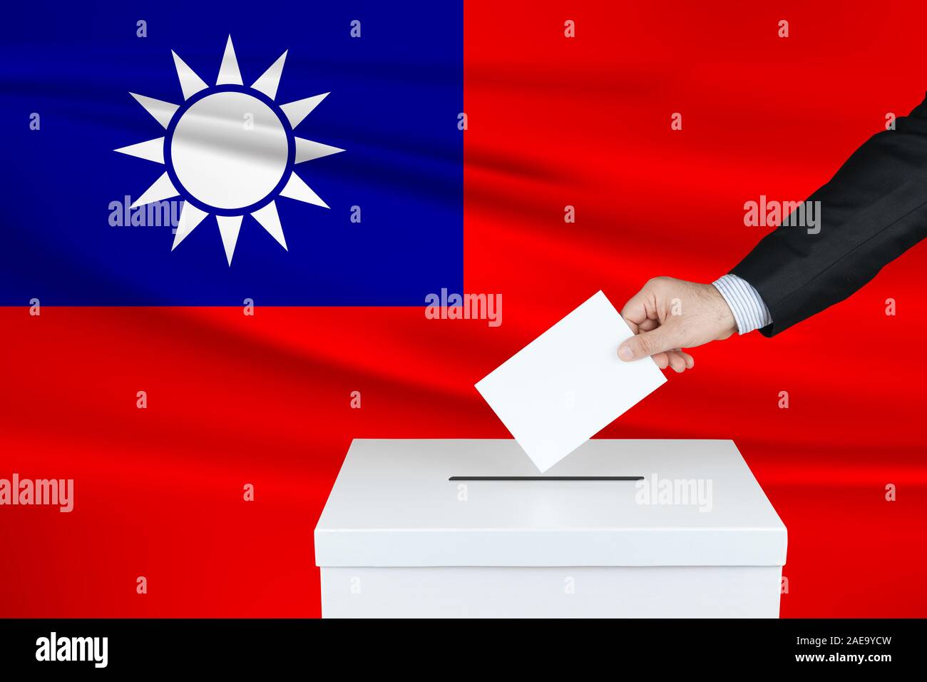 Election in Taiwan. The hand of man putting his vote in the ballot box. Waved Taiwan flag on background. Stock Photo