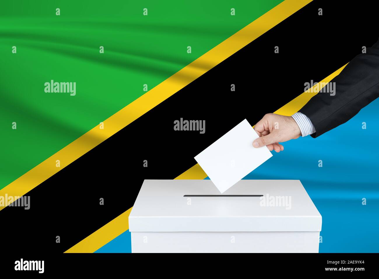 Election in Tanzania. The hand of man putting his vote in the ballot box. Waved Tanzania flag on background. Stock Photo
