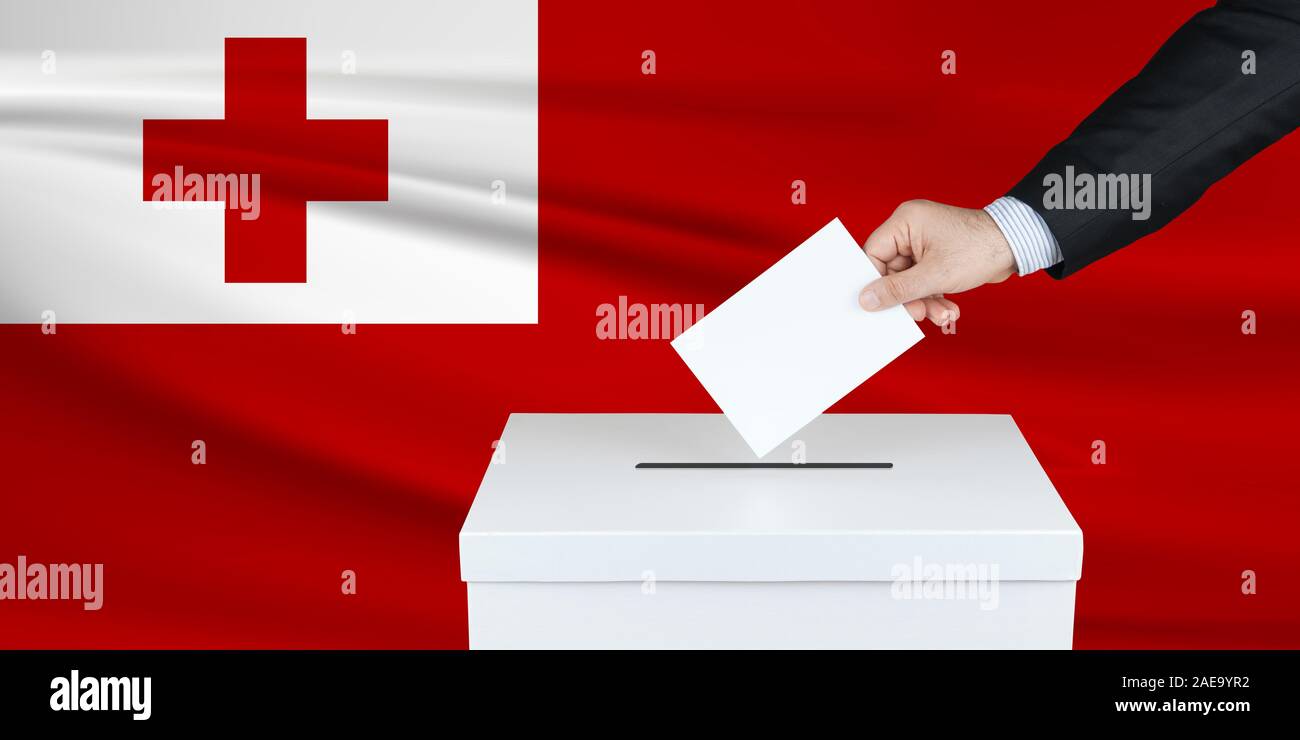 Election in Tonga. The hand of man putting his vote in the ballot box. Waved Tonga flag on background. Stock Photo
