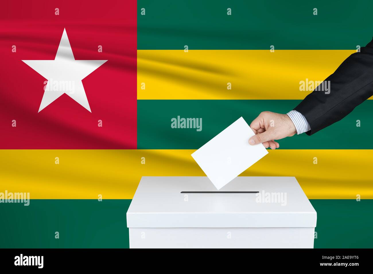 Election in Togo. The hand of man putting his vote in the ballot box. Waved Togo flag on background. Stock Photo