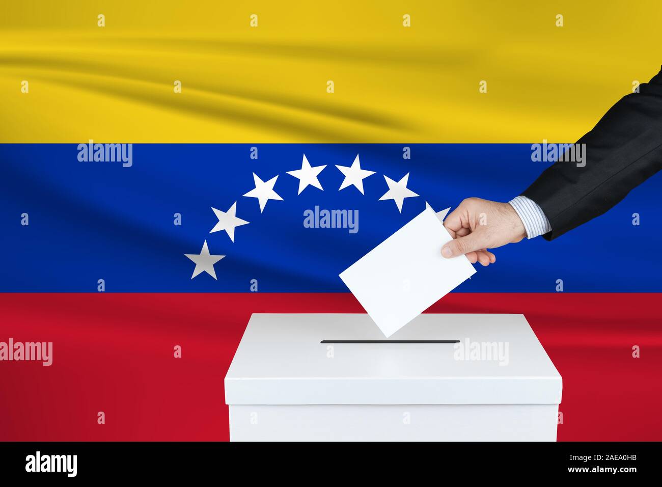 Election in Venezuela. The hand of man putting his vote in the ballot box. Waved Venezuela flag on background. Stock Photo