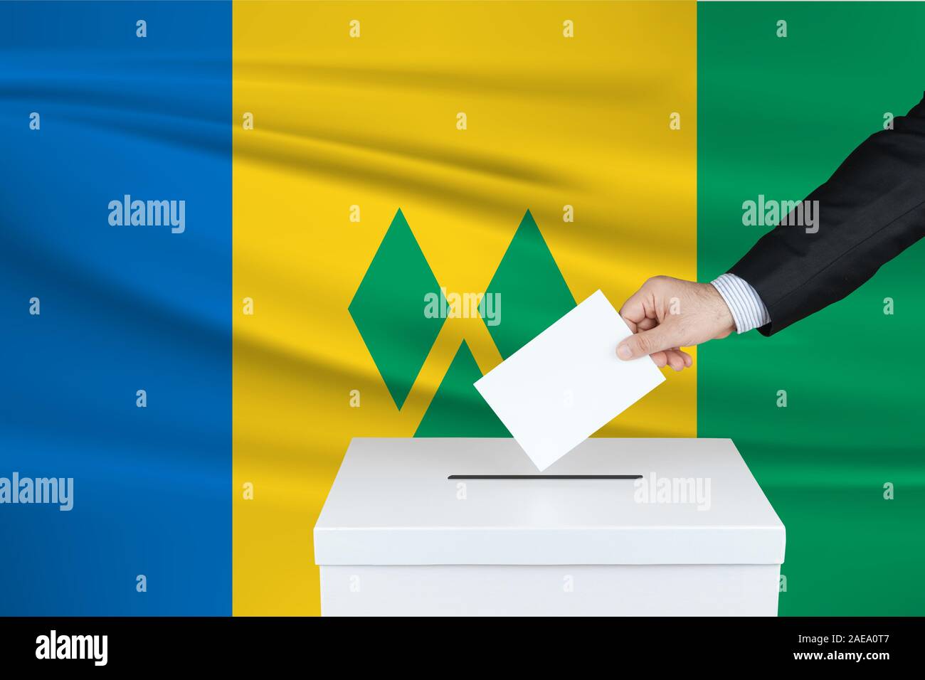 Election in Vincent. The hand of man putting his vote in the ballot box. Waved Vincent flag on background. Stock Photo