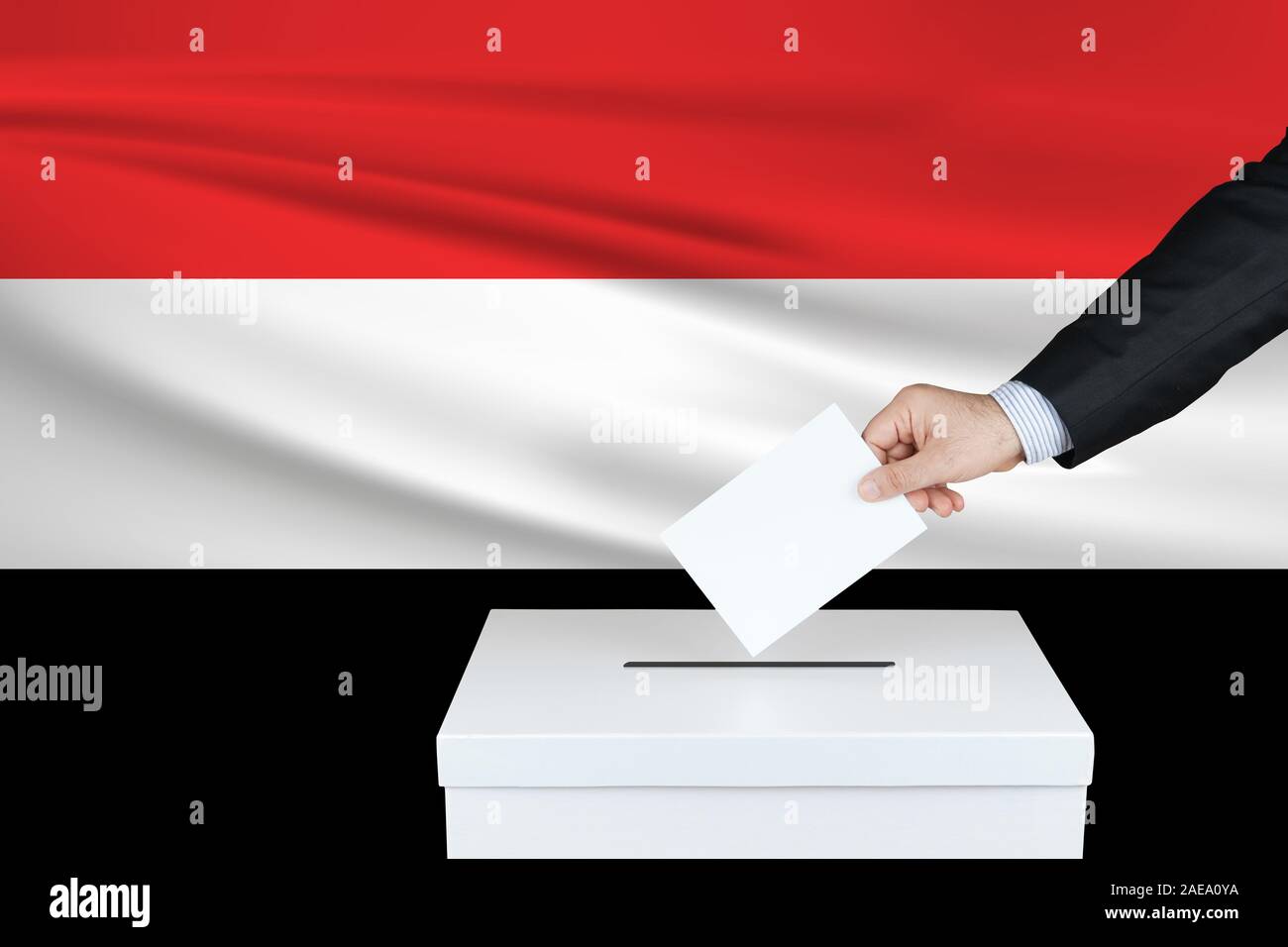 Election in Yemen. The hand of man putting his vote in the ballot box. Waved Yemen flag on background. Stock Photo