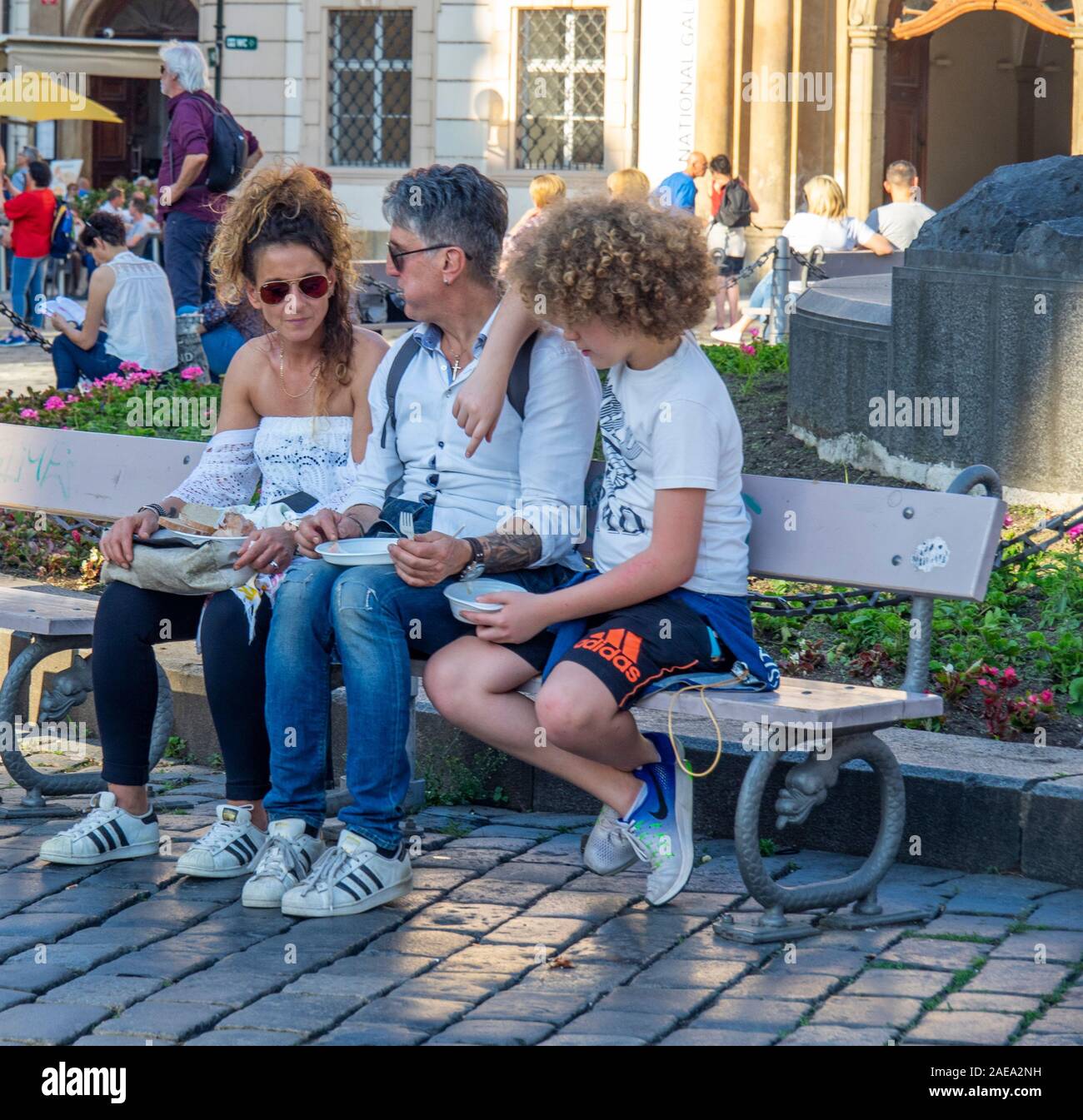 Family of mother father and son sitting on a bench having a snack in Old Town Square Prague Czech Republic. Stock Photo