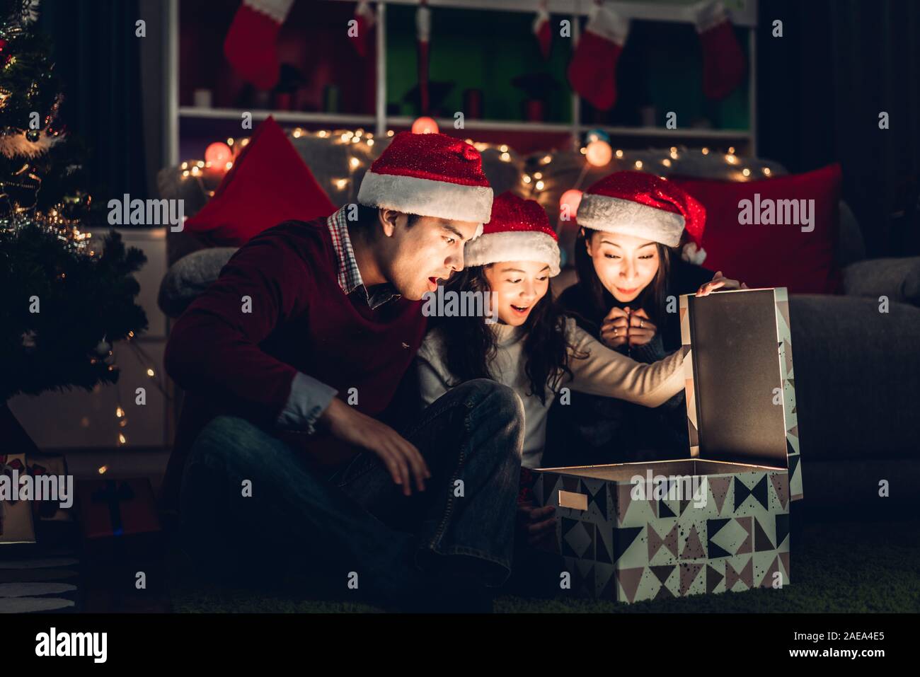 Portrait of happy family father and mother with daughter in santa hats having fun opening magic christmas gift box and enjoying spending time together Stock Photo