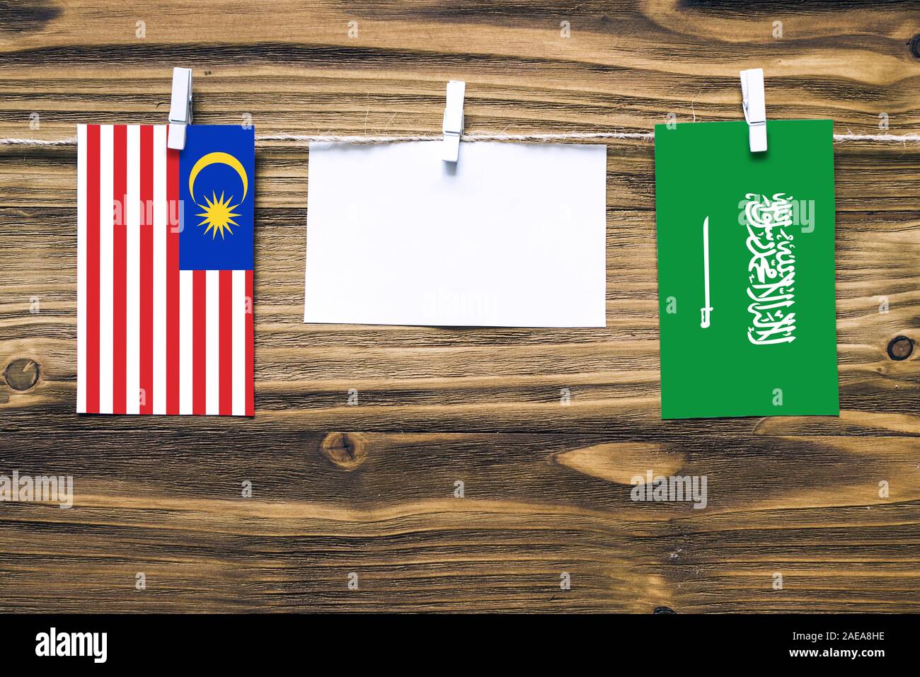Hanging flags of Malaysia and Saudi Arabia attached to rope with clothes pins with copy space on white note paper on wooden background.Diplomatic rela Stock Photo