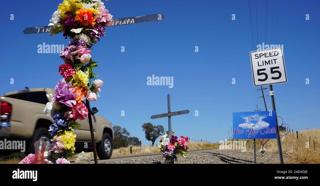 Roadside car accident memorials with flowers and speed limit sign with pickup truck driving by in Tuolumne County, California. Stock Photo