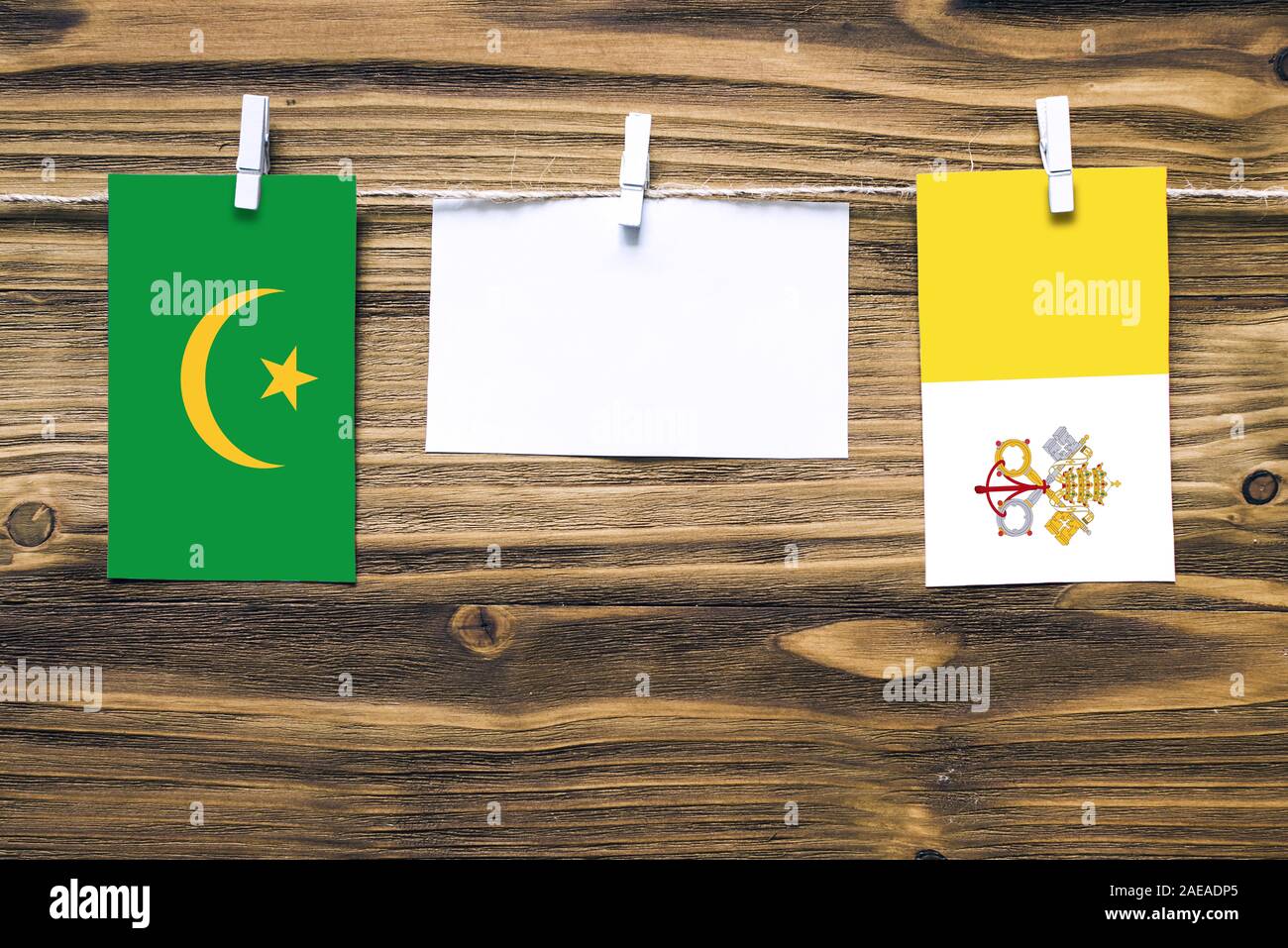 Hanging flags of Mauritania and Vatican City attached to rope with clothes pins with copy space on white note paper on wooden background.Diplomatic re Stock Photo