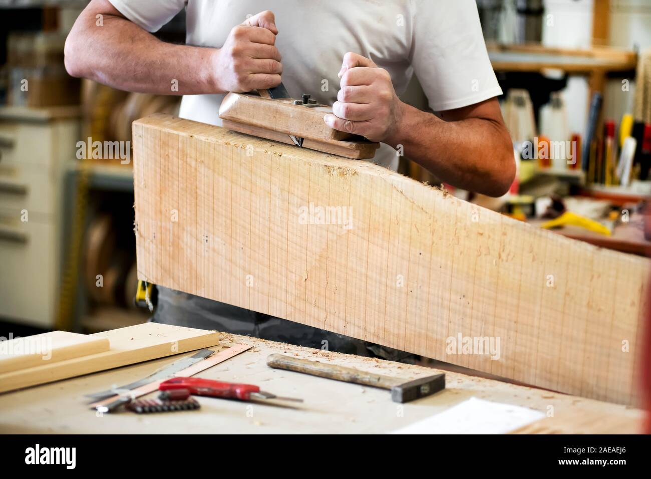 Carpenter working with a planer on a block of wood smoothing the surface in a close up of his hands and tools on the workbench Stock Photo