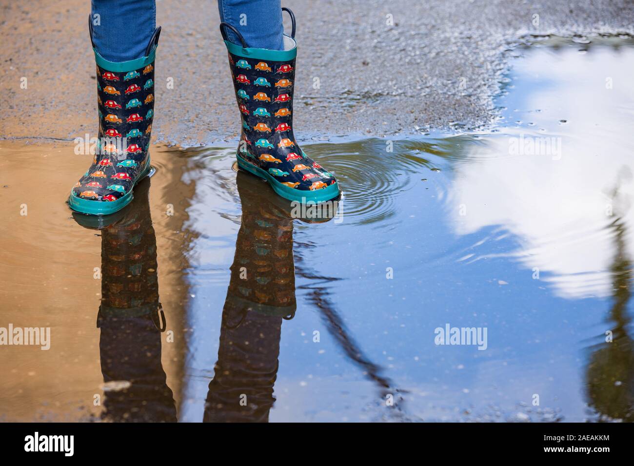 Kid boy in funny rubber boots standing in the puddle in the street ...