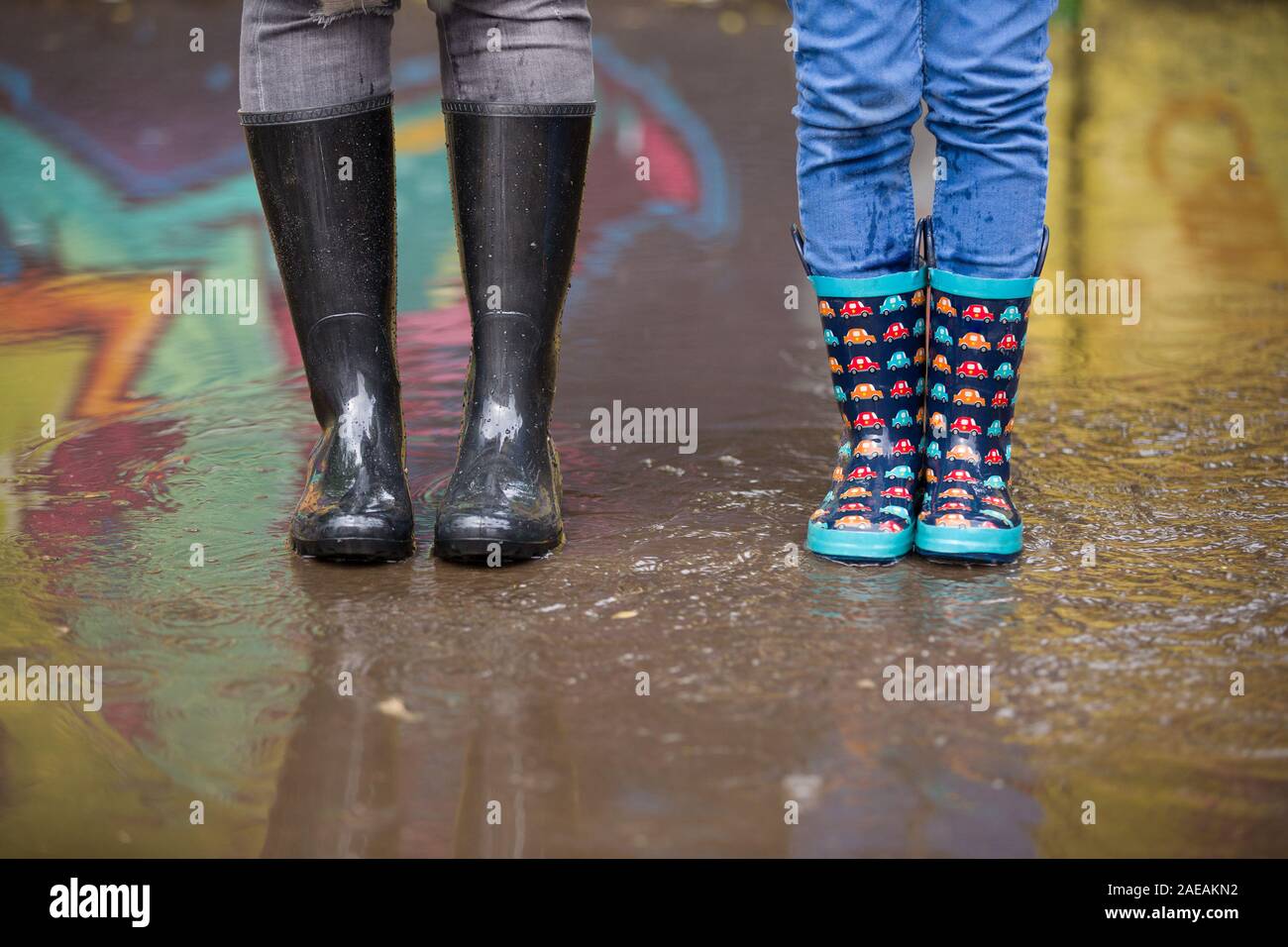 Kid boy and woman in funny rubber boots standing in the puddle in the ...
