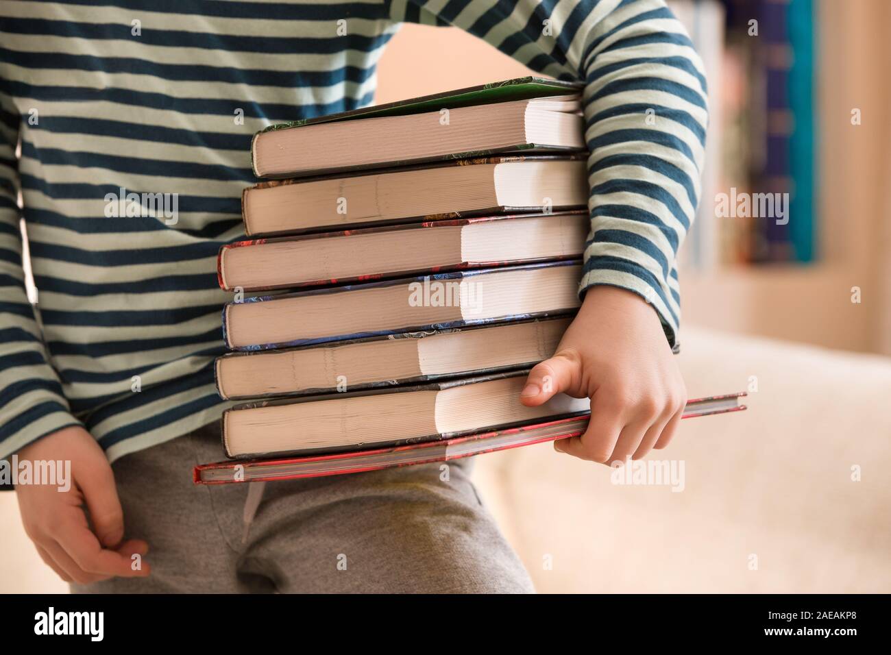 Little boy in a striped shirt holding a pile of books. Education and knowledge concept. Reading children. Back to school. Happy reading. Schoolboy at Stock Photo