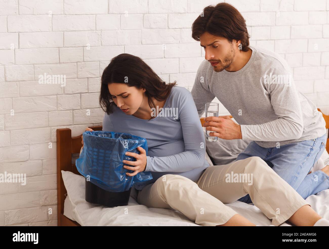 Pregnant woman suffering from morning sickness, vomiting to garbage can Stock Photo