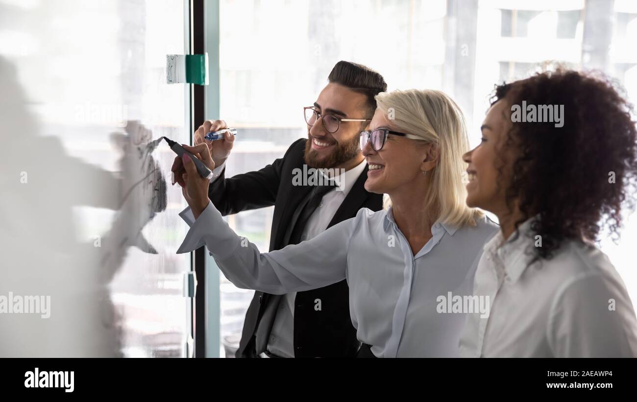 Smiling diverse colleagues brainstorm writing on whiteboard Stock Photo