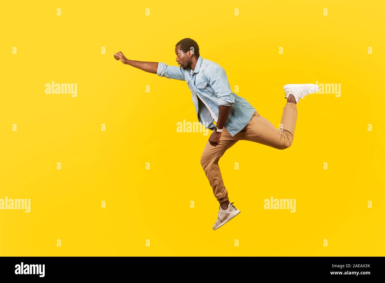 Full length portrait of serious cool handsome man in denim casual shirt jumping in air or flying high with one stretched arm, feeling to be superman. Stock Photo