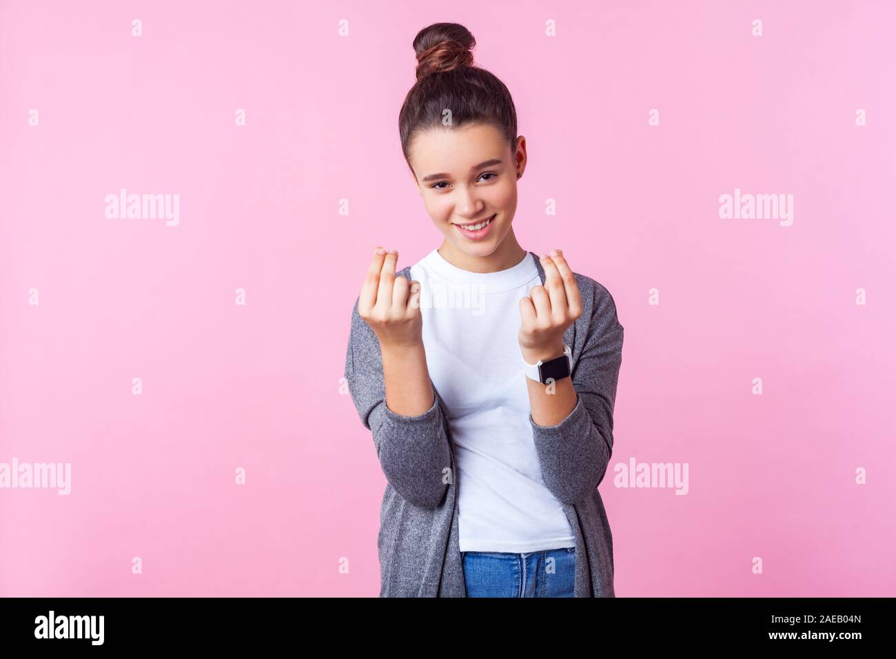 Portrait of sly brunette girl with bun hairstyle in casual clothes showing money gesture and looking cunning at camera, teenager demanding more allowa Stock Photo