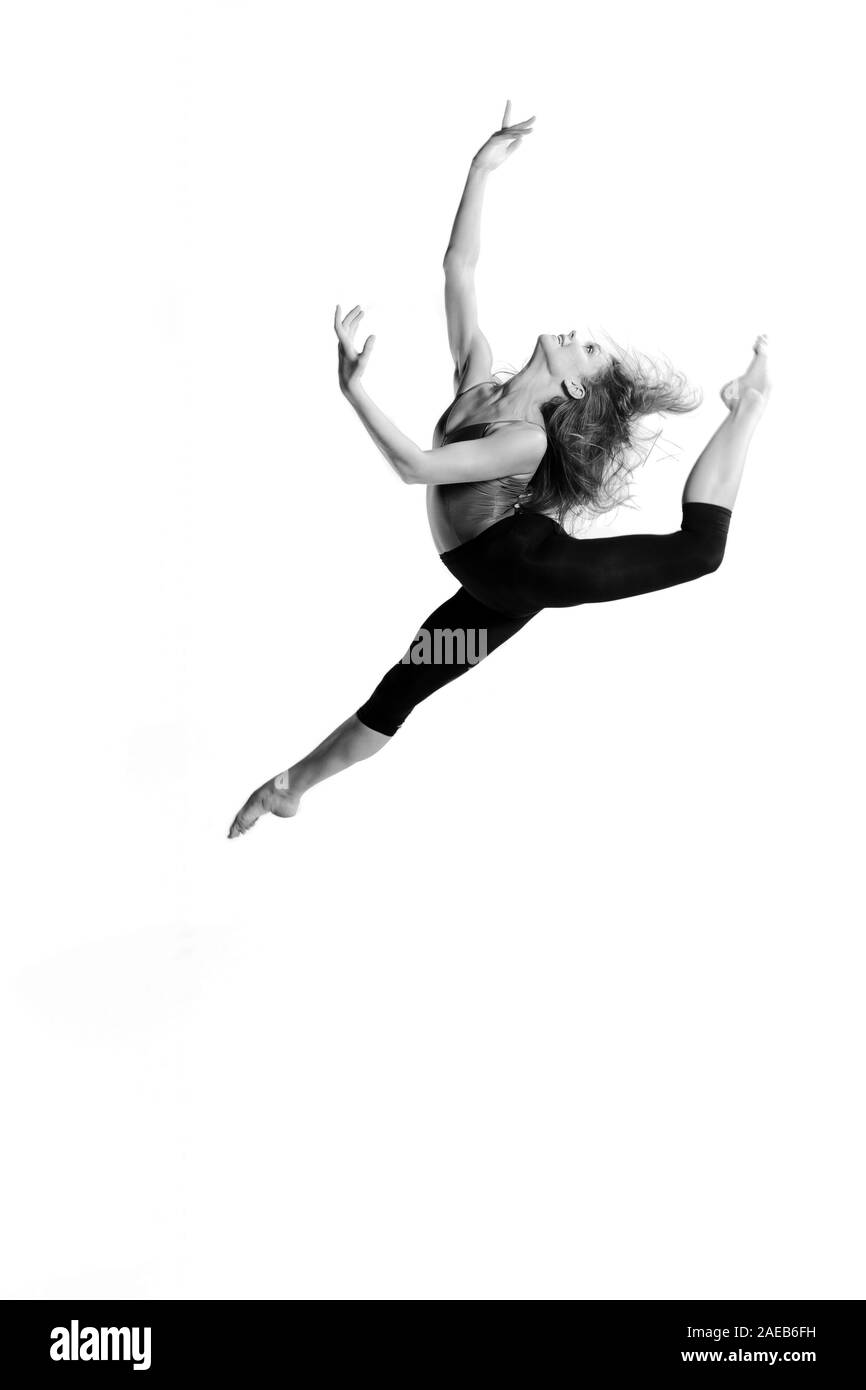 Ballerina with open long hair jumps in the air in front of white background. Black and white picture. Stock Photo