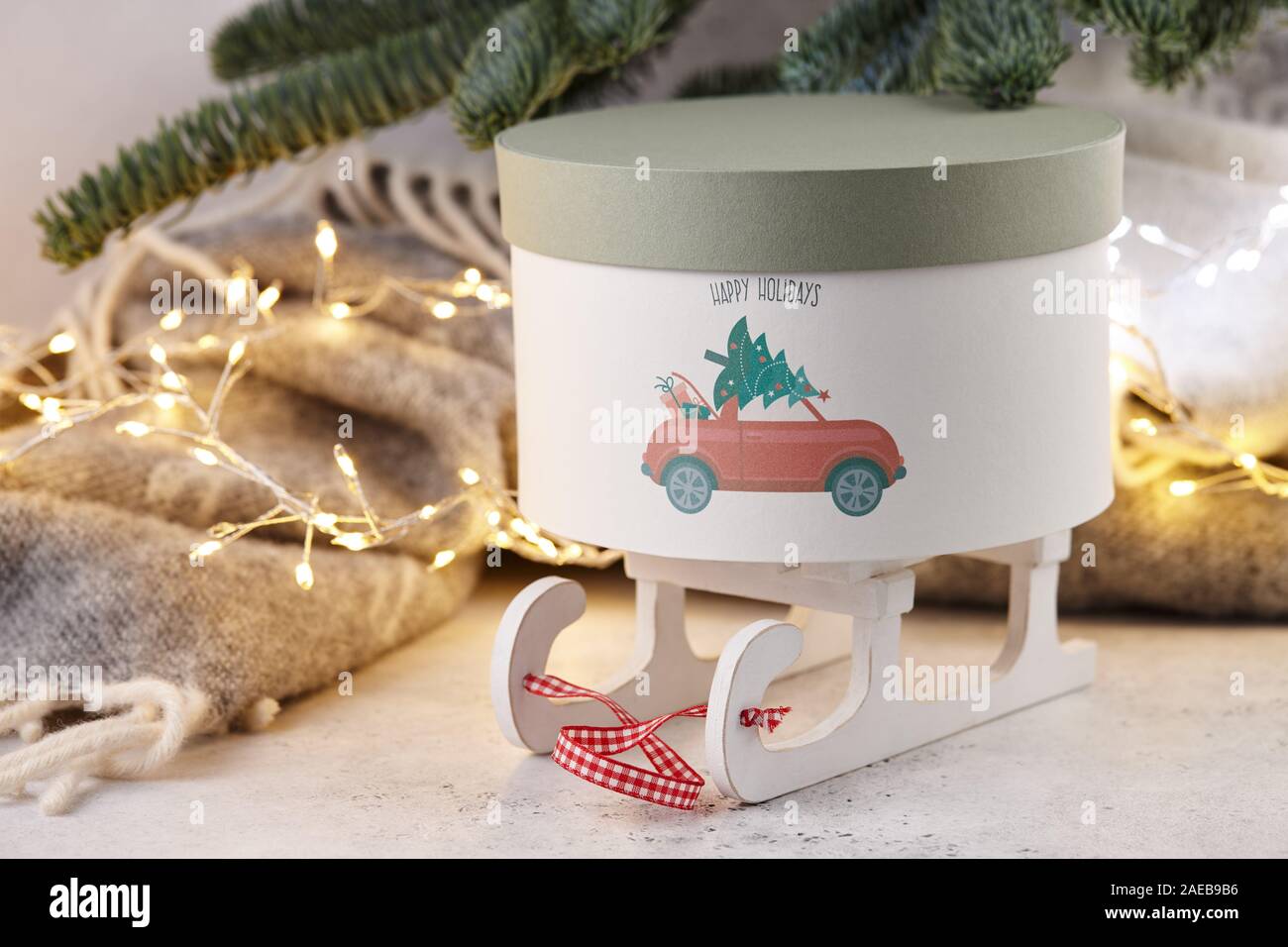 Gift box with holiday car print under Christmas tree on wool blanket and lights background Stock Photo