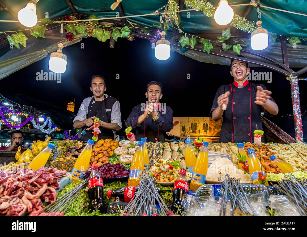Cheerful, singing street food vendors recommends culinary delights at night in Jemaa el-Fnaa or Djema El-Fna market square.Marrakesh,Morocco. Stock Photo