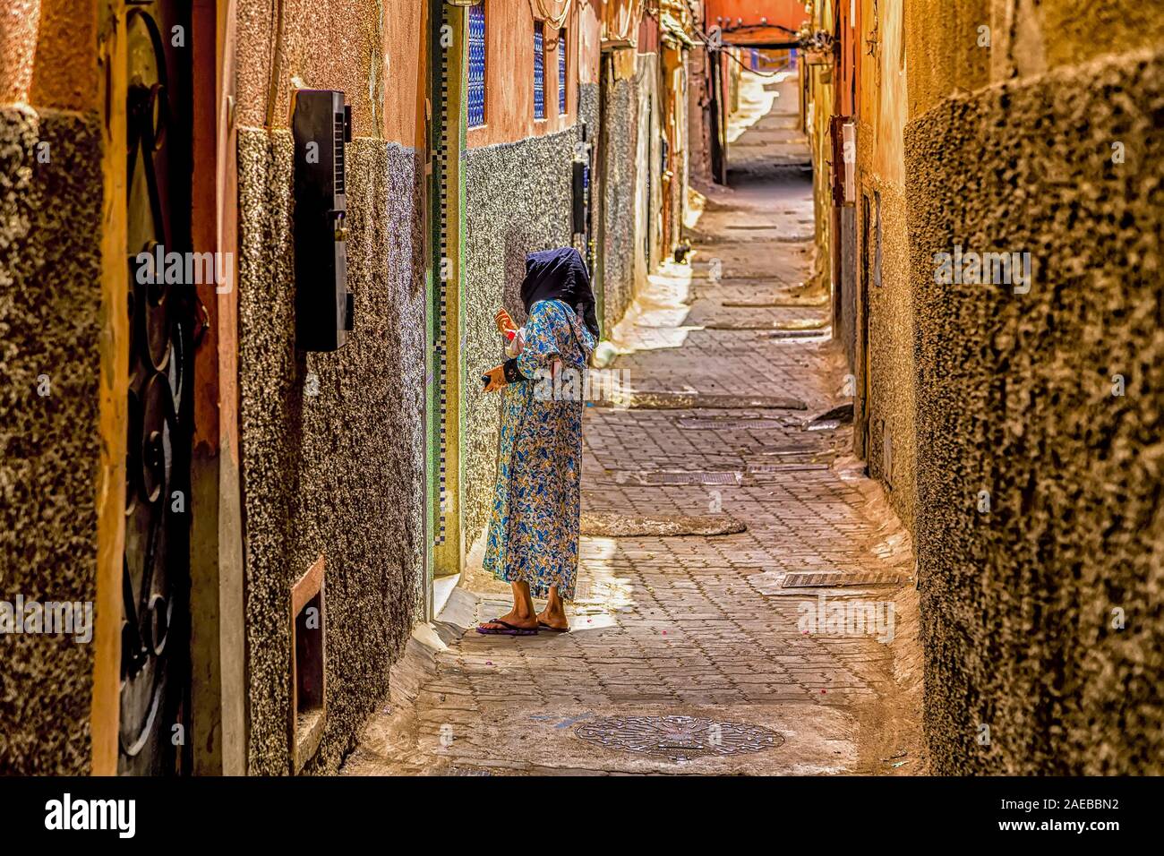Arab woman talking in the characteristic narrow alley of Marrakesh Medina, with her invisible neighbour behind the door. Stock Photo