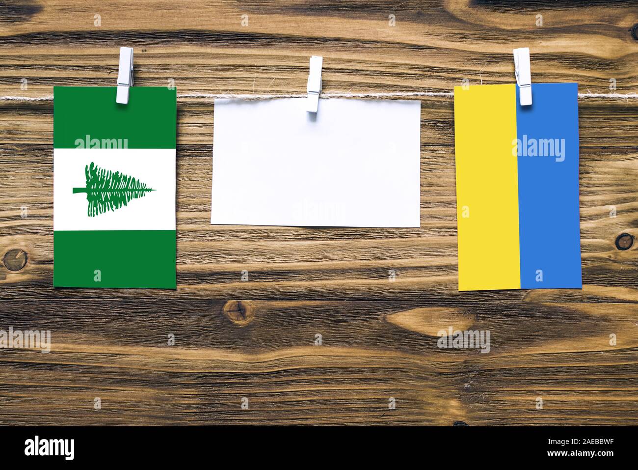 Hanging flags of Norfolk Island and Ukraine attached to rope with clothes pins with copy space on white note paper on wooden background.Diplomatic rel Stock Photo