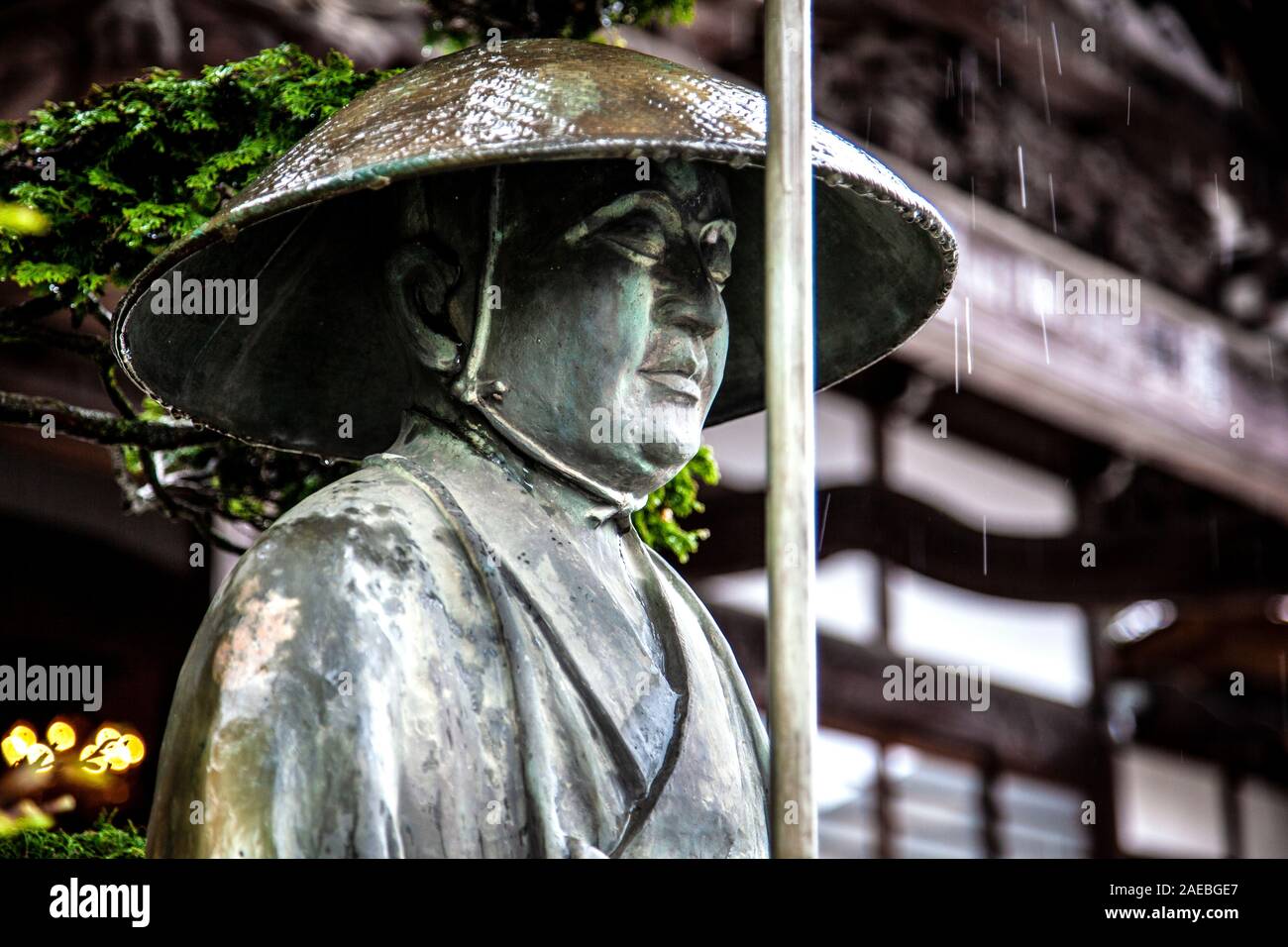 Statue of a man in a hat outside Baigan-ji Temple in rainy Ome, Tokyo, Japan Stock Photo