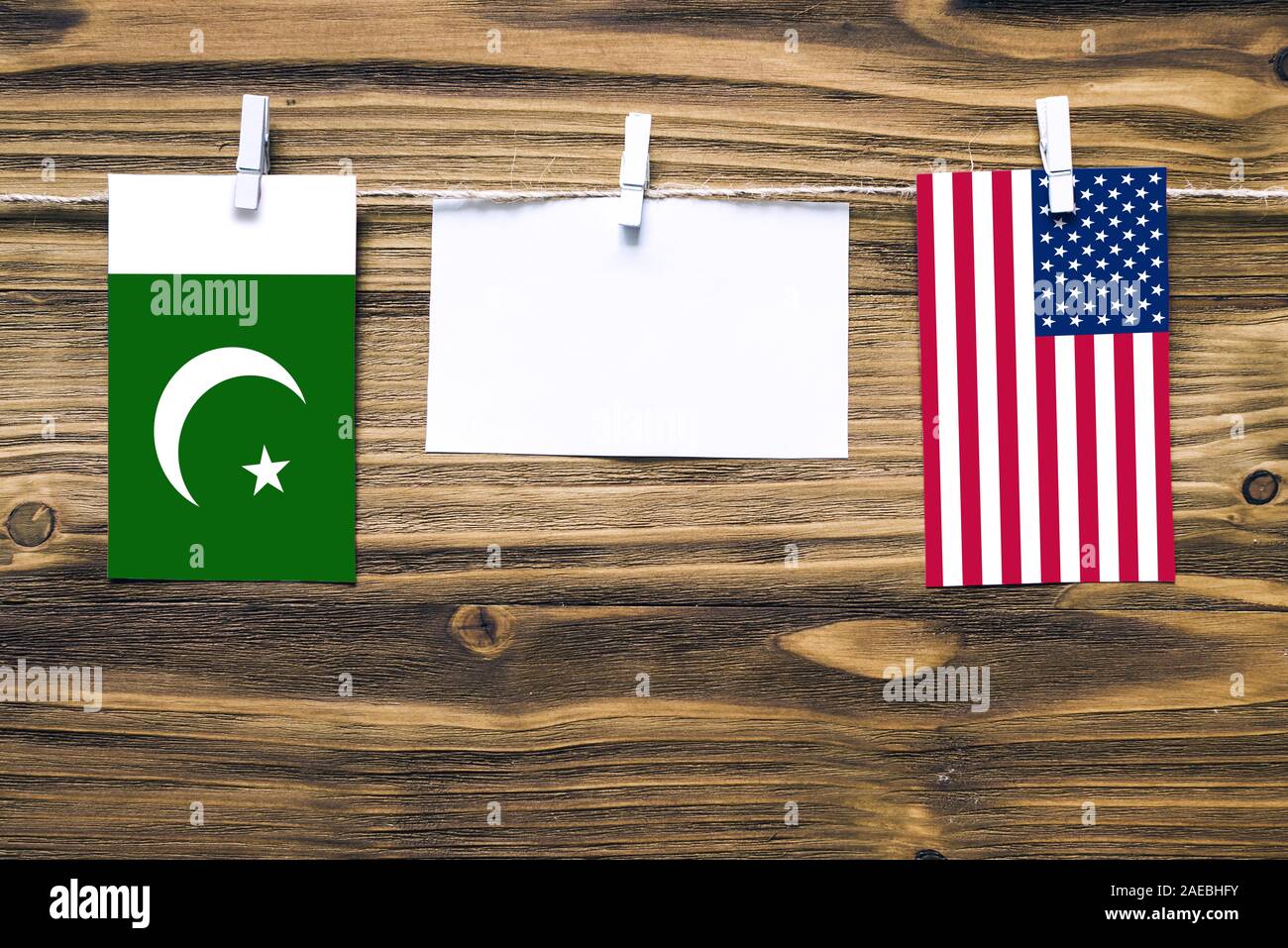 Hanging flags of Pakistan and United States attached to rope with clothes pins with copy space on white note paper on wooden background.Diplomatic rel Stock Photo