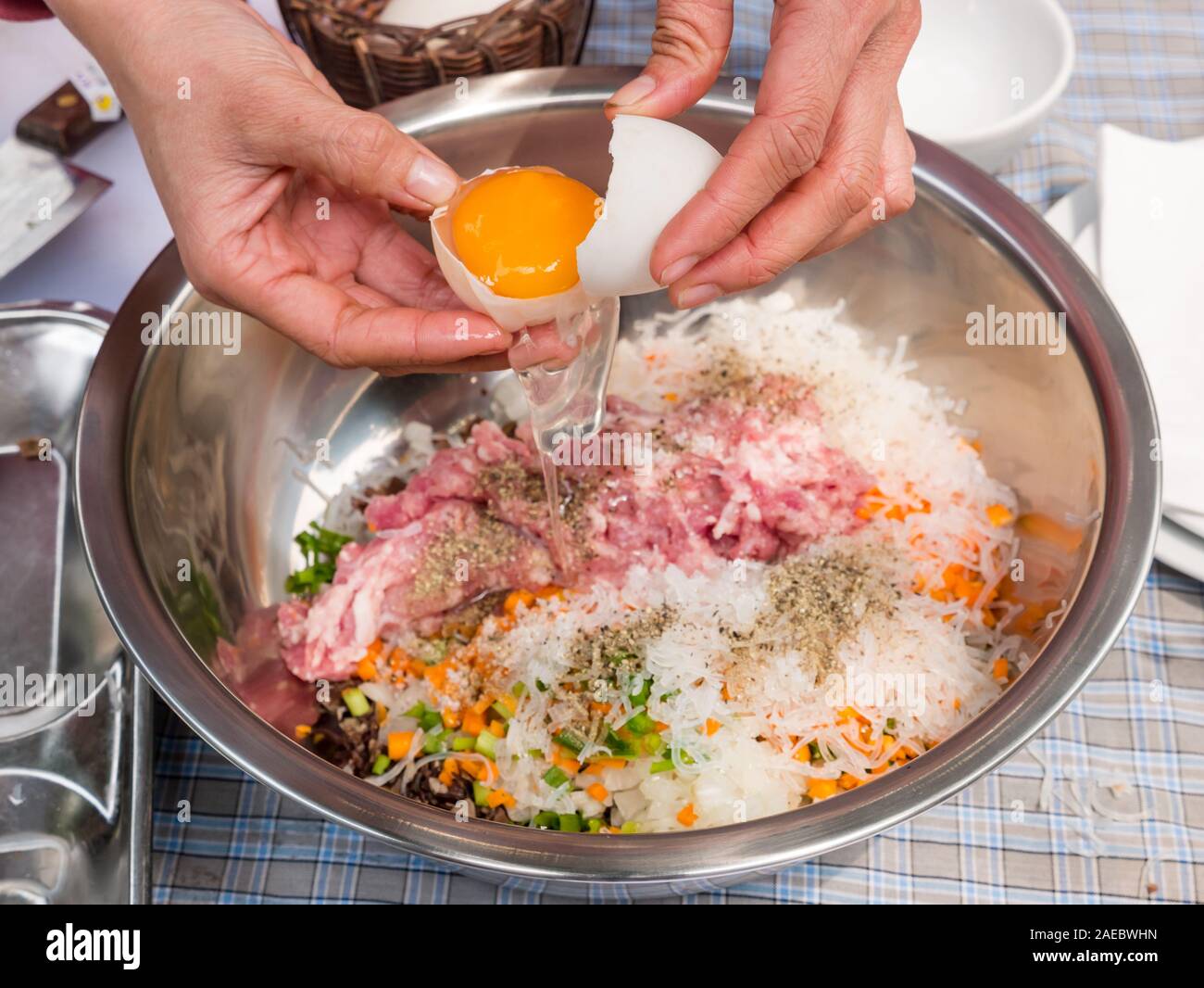 Mixing bowl with ingredients for pork mince spring rolls, with hands breaking egg, Vietnam, Asia Stock Photo