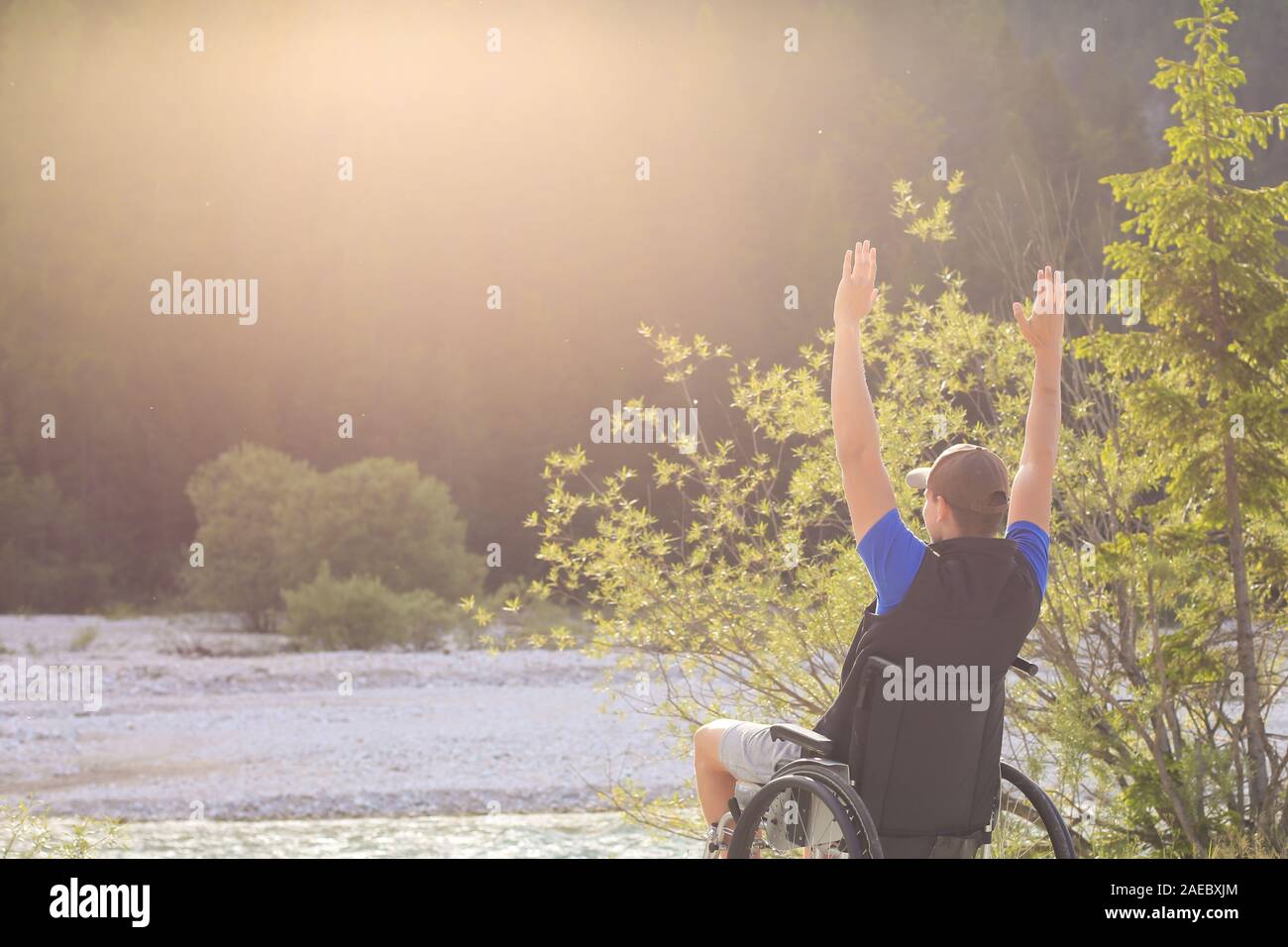 Happy and joyfull young man in wheelchair outside in nature on a sunny summer day with his hands raised up. Stock Photo