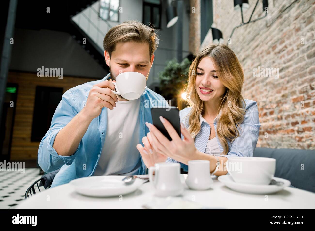 Young lovely couple surfing the web and looking at photos on mobile phone. In a cafe, hotel ar waiting room Stock Photo