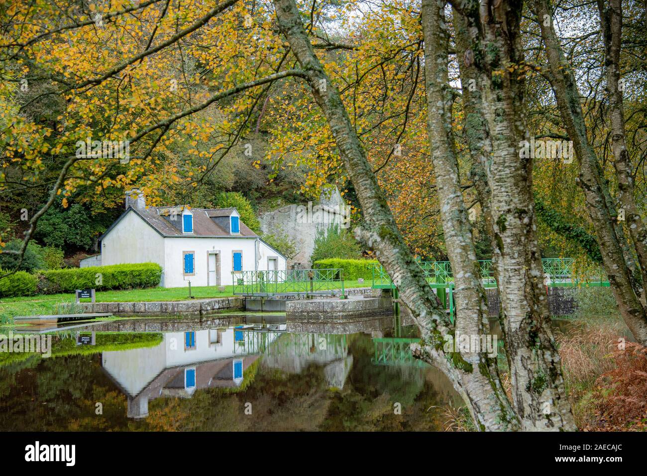 Autumn on the canal from Nantes to Brest. A small white lock house is reflected in the water at the edge of a lock Stock Photo