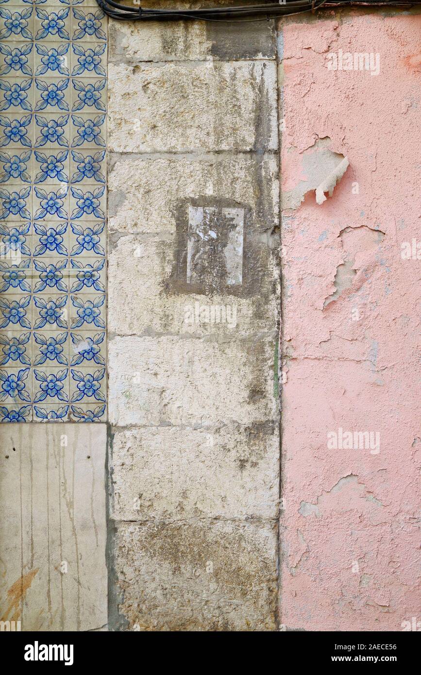 Front view of an old wall with faded blue ceramic tiles (azulejos), dirty and weathered stone blocks and pink paint peeling off. Textured background Stock Photo