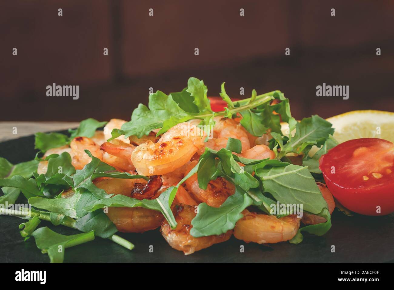 Fresh homemade salad of shrimp, arugula and tomato on a black slate dish, close-up. Stock Photo