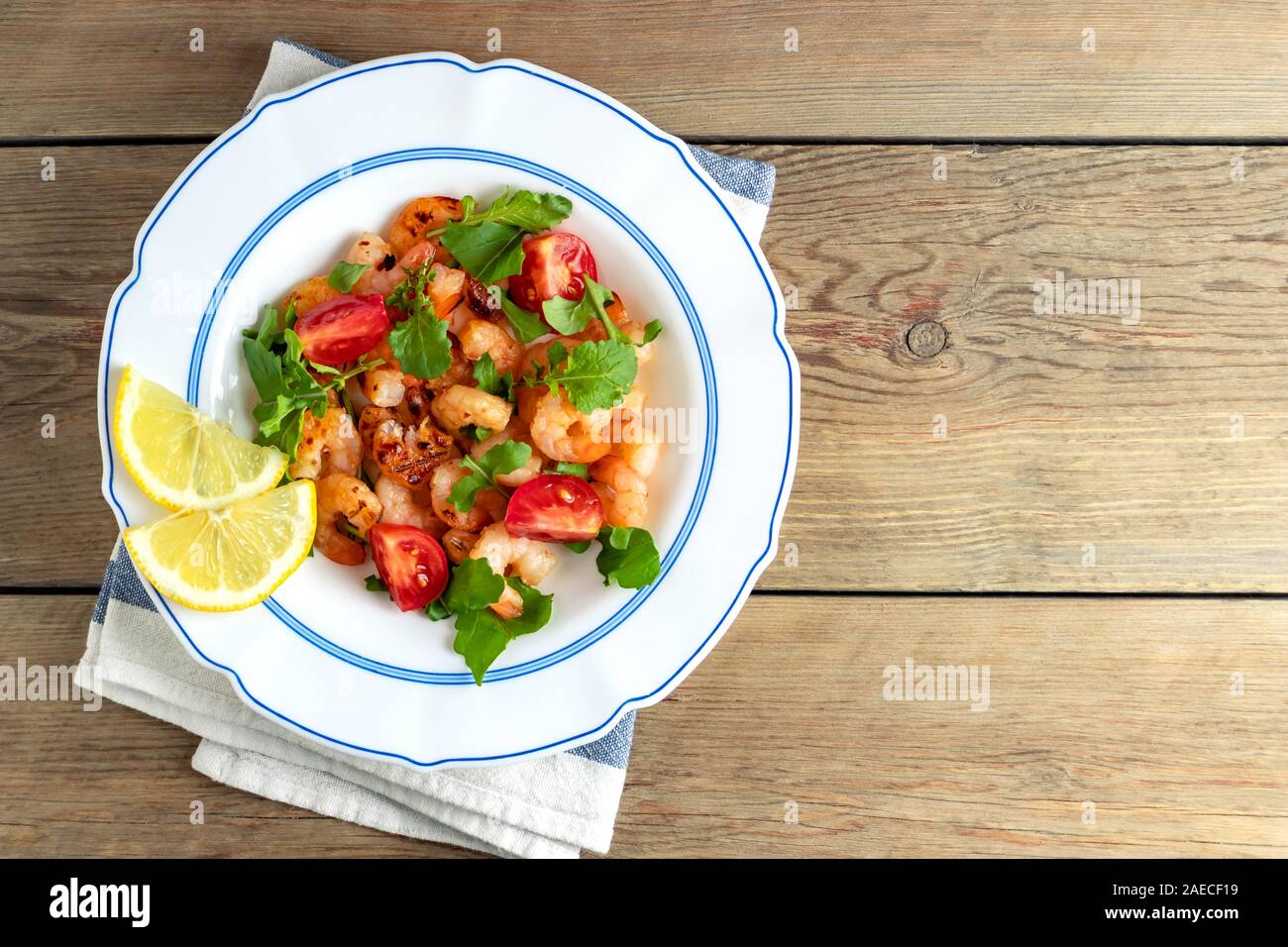 Fresh homemade salad of shrimp, arugula and tomato in a white plate on a wooden table, top view, flat lay, copyspace. Stock Photo