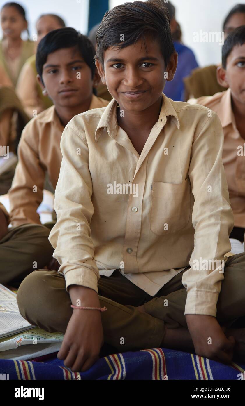Indian primary school student sits cross-legged on the floor, during lesson time, smiling for the camera, Rajasthan, India, Asia. Stock Photo