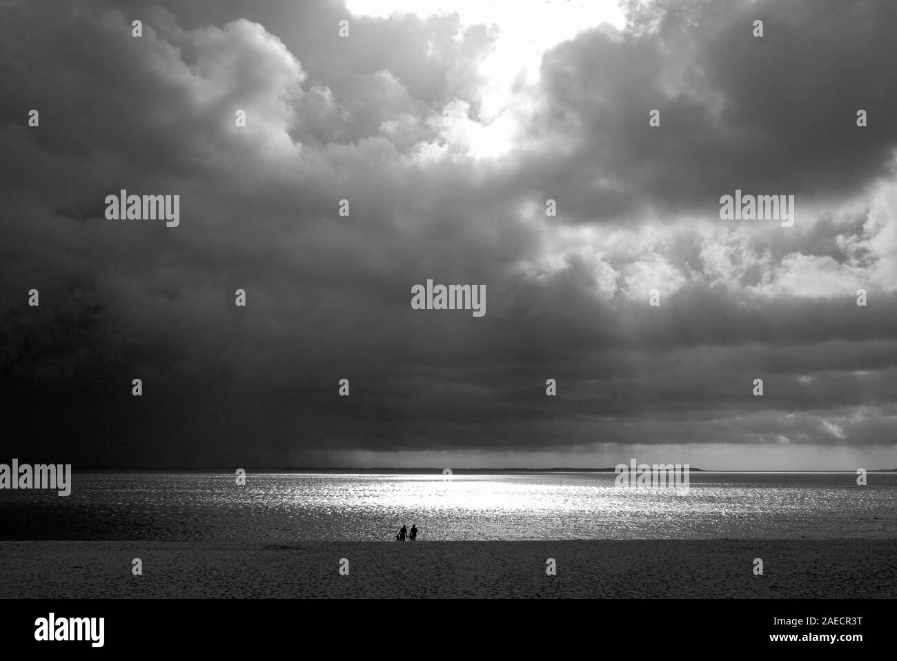 Paar am Strand bei Hoernum unter dunklen Regenwolken vor hellem Sonnenlicht Stock Photo