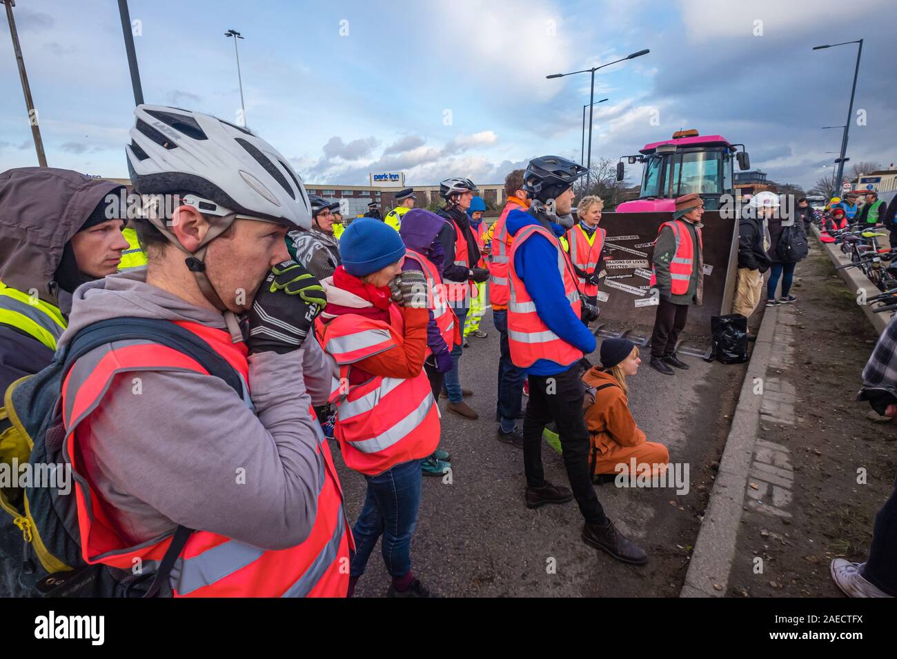 London, UK. 8th December 2019. Extinction Rebellion protesters listen at the end of the lie-in protest against airport expansion in front of a bulldozer on the Heathrow roundabout echoing Boris Johnson's promised he would lie down with John McDonnell 'in front of those bulldozers and stop the construction of that third runway'. XR brought the bulldozer, but Boris didn't turn up. Police stopped them going to the Heathrow roundabout and instead the protest blocked one lane of the A4. Peter Marshall/Alamy Live News Stock Photo