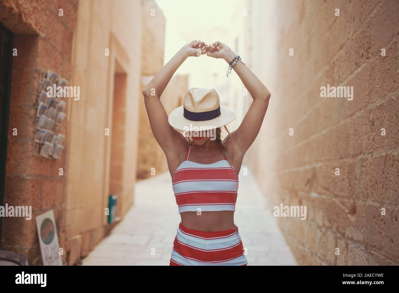 Young positive woman in hat hands up on Mediterranean street Stock Photo