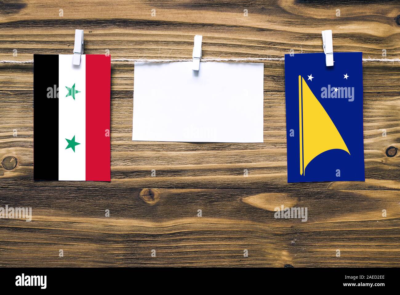 Hanging flags of Syria and Tokelau attached to rope with clothes pins with copy space on white note paper on wooden background.Diplomatic relations be Stock Photo