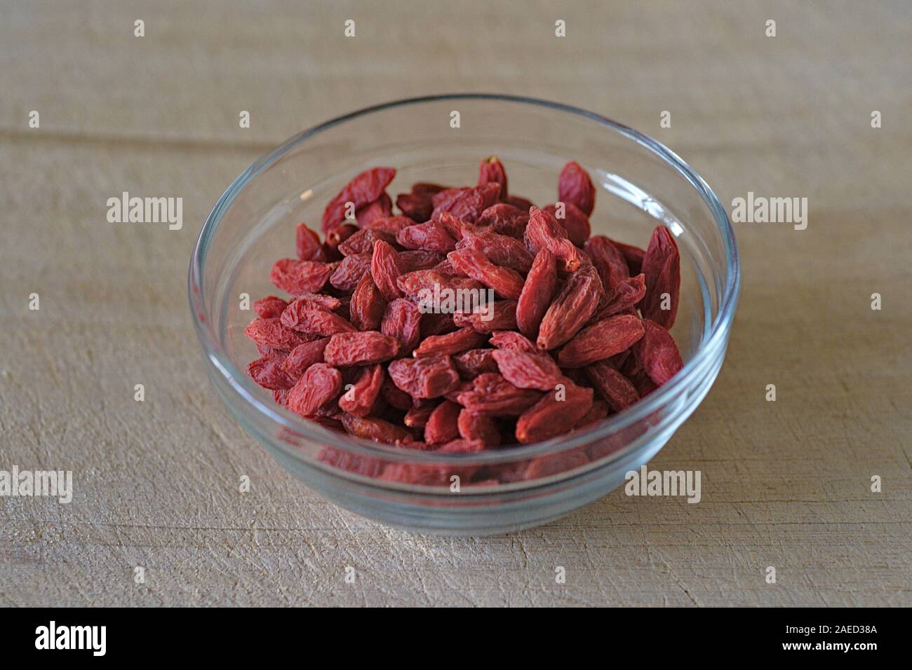 Dried Goji Berries (Lycium barbarum) in a small glass bowl on a wooden chopping board. Stock Photo