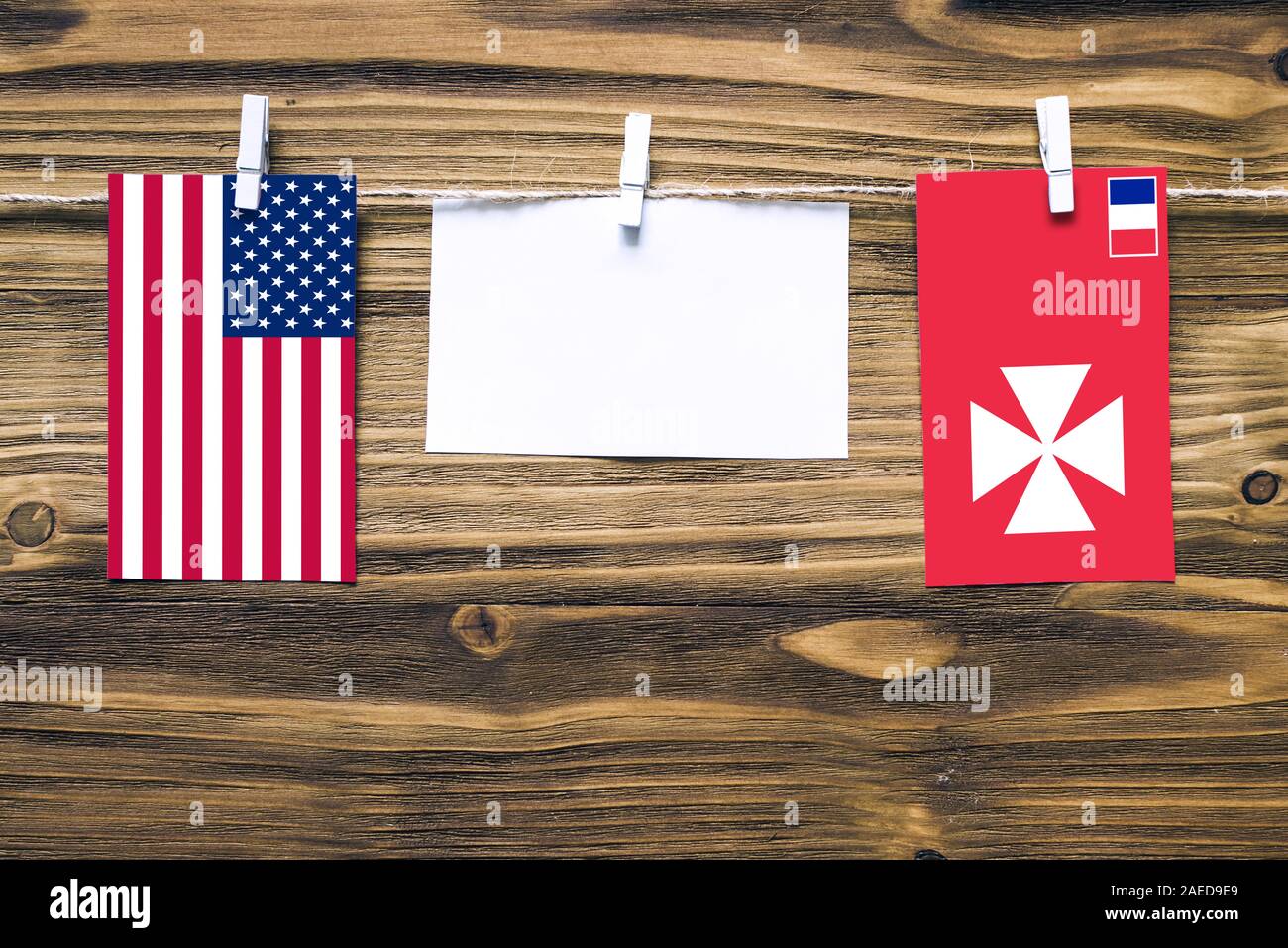 Hanging flags of United States and Wallis And Futuna attached to rope with clothes pins with copy space on white note paper on wooden background.Diplo Stock Photo