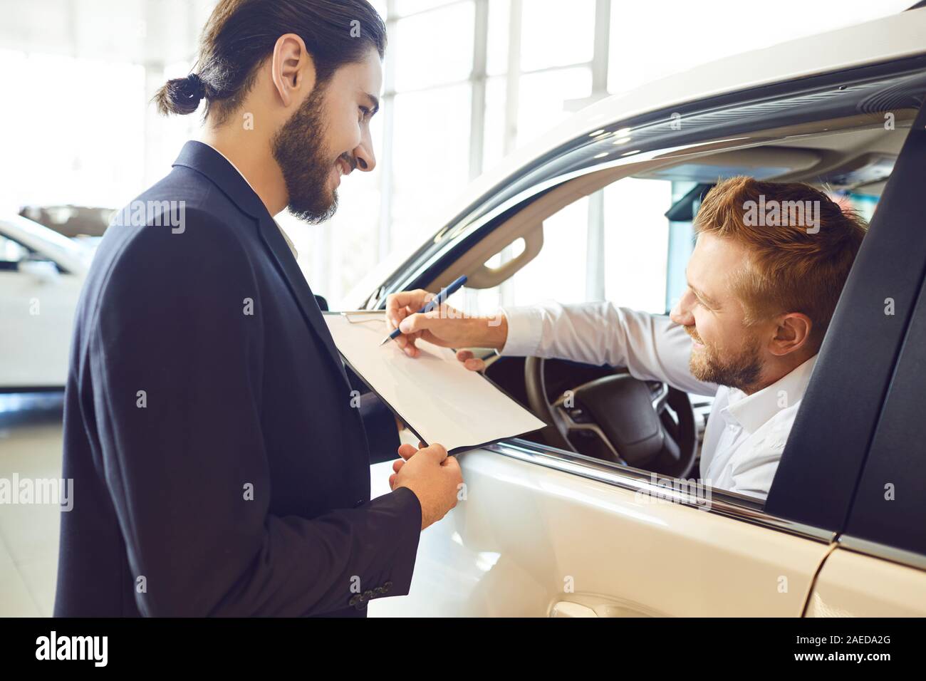 A young woman buys a car signs a contract in a car showroom. A man signs a car rental agreement. Stock Photo