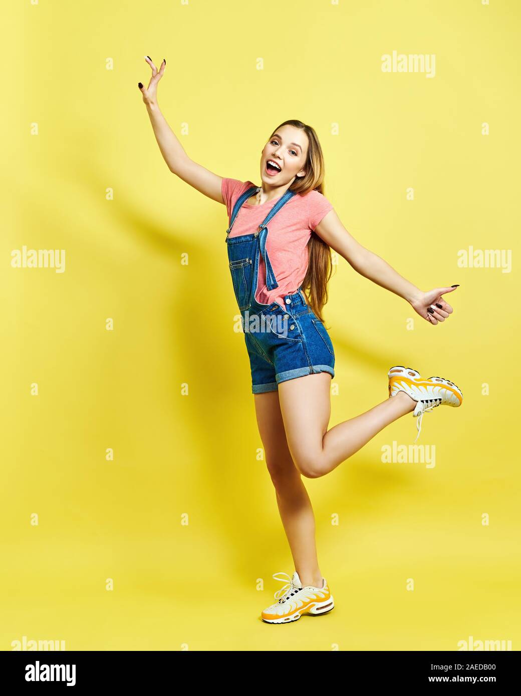 Girlish, funky, happiness, dream, fun, joy, summer concept. Very excited happy cute girl is jumping up, in summer outfit, on yellow background Stock Photo