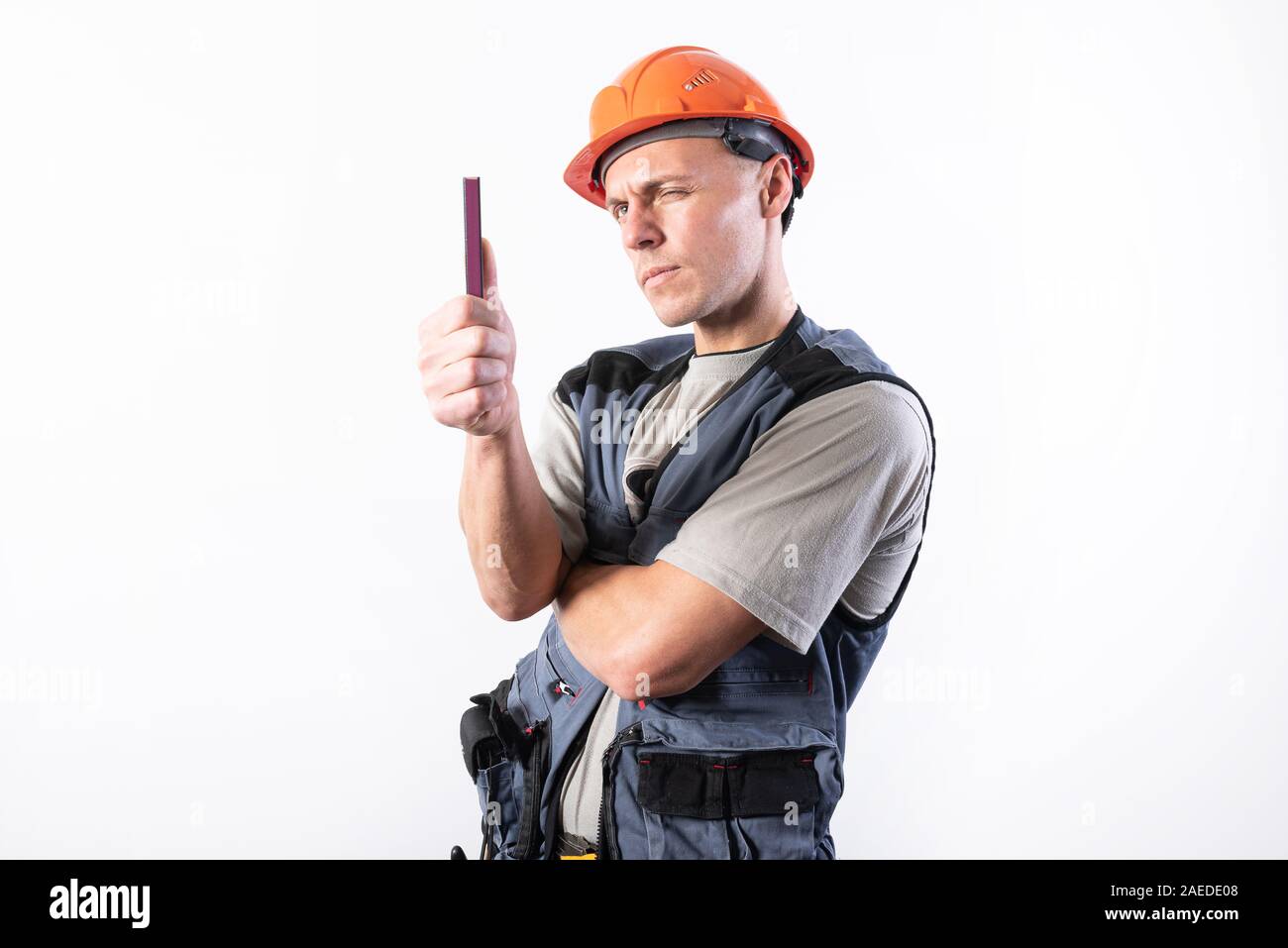 A builder in a helmet makes visual measurement with a marking pencil. Stock Photo