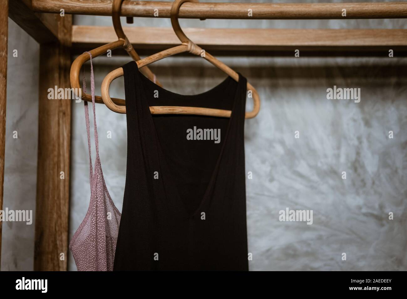Little black dress hanging on a  clothing rack, rappan wooden hangers. Boho chic style. Fashion blogging concept, neutral colors. Loft bedroom interio Stock Photo