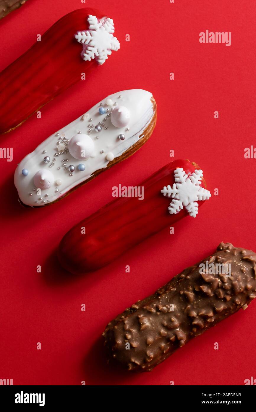 Red glazed eclair with white snowflakes on red colored background. Copyspace, flat lay, overhead, minimalist food photography concept. Christmas desse Stock Photo