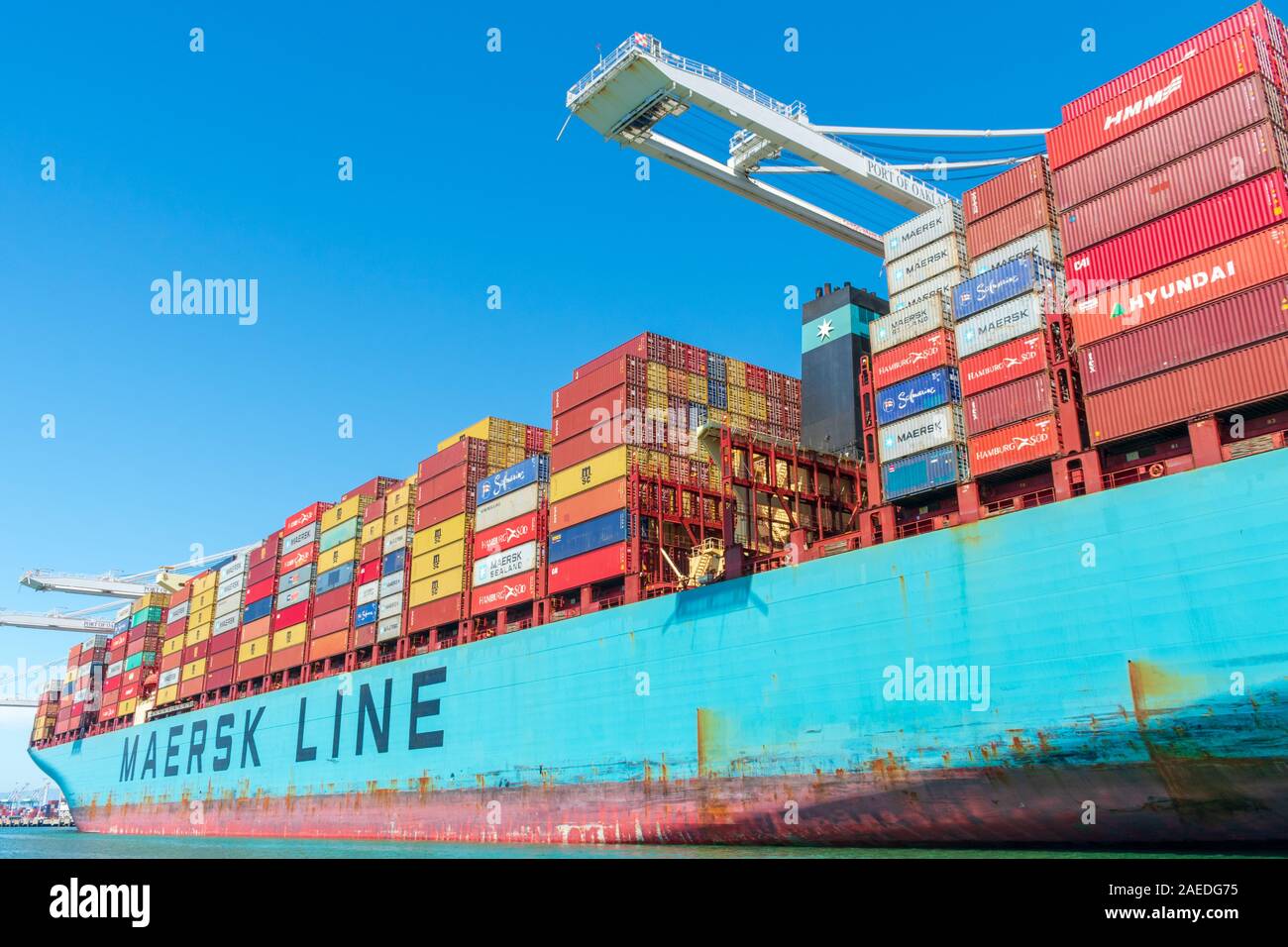 Colorful cargo shipping containers stacked aboard of container ship Maersk Line during cargo loading and unloading operation under blue sky - Oakland, Stock Photo