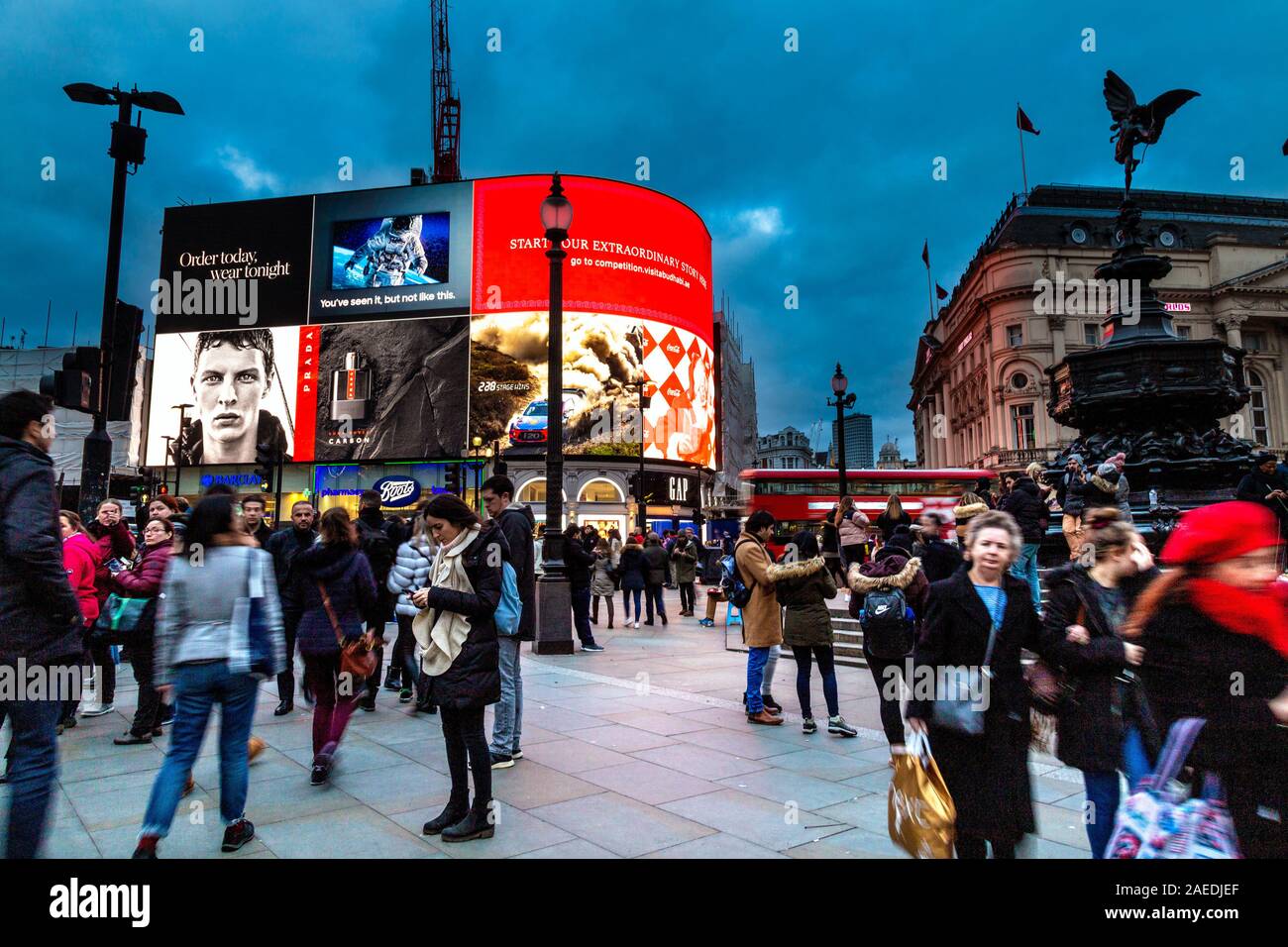 People rushing around at Piccadilly Circus at evening time with the iconic advertising screen in the background, London, UK Stock Photo