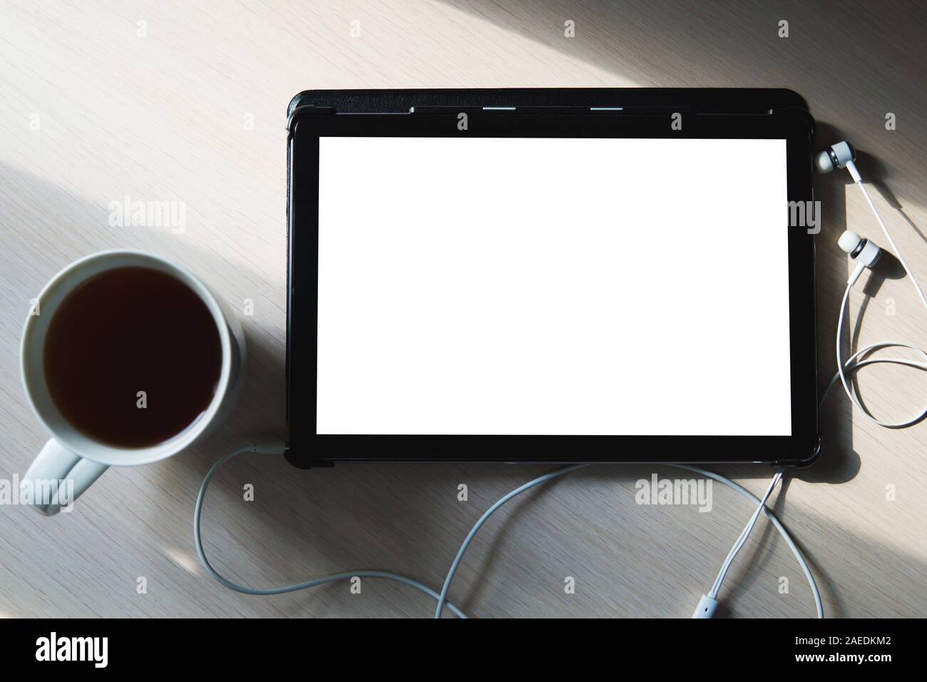 A blank tablet, earphones and a cup of tea on the wooden table. Business and education background. Flat lay, copy space, view from above. Stock Photo