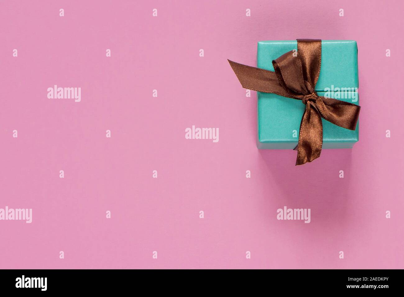 Turquoise gift or present box with brown ribbon on pink table top view ...